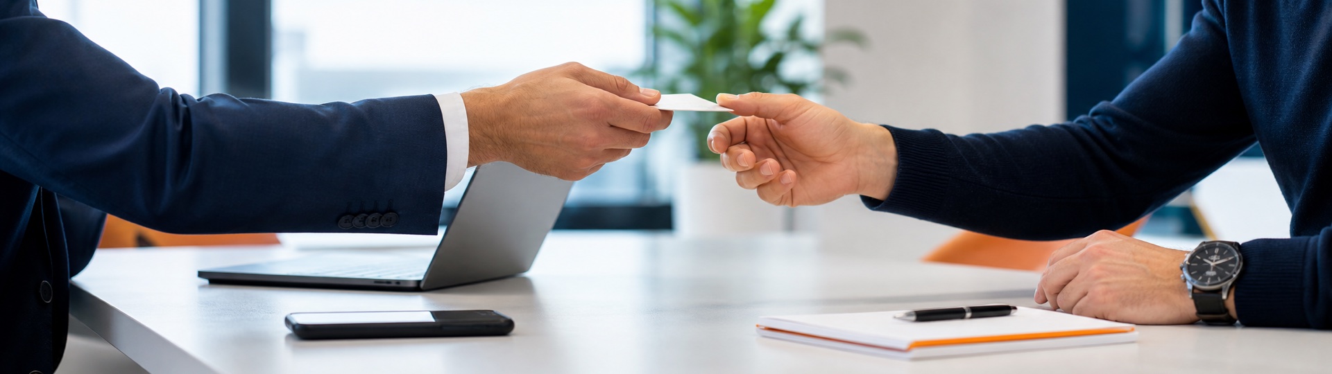 Two professionals exchanging a business card in a bright office.